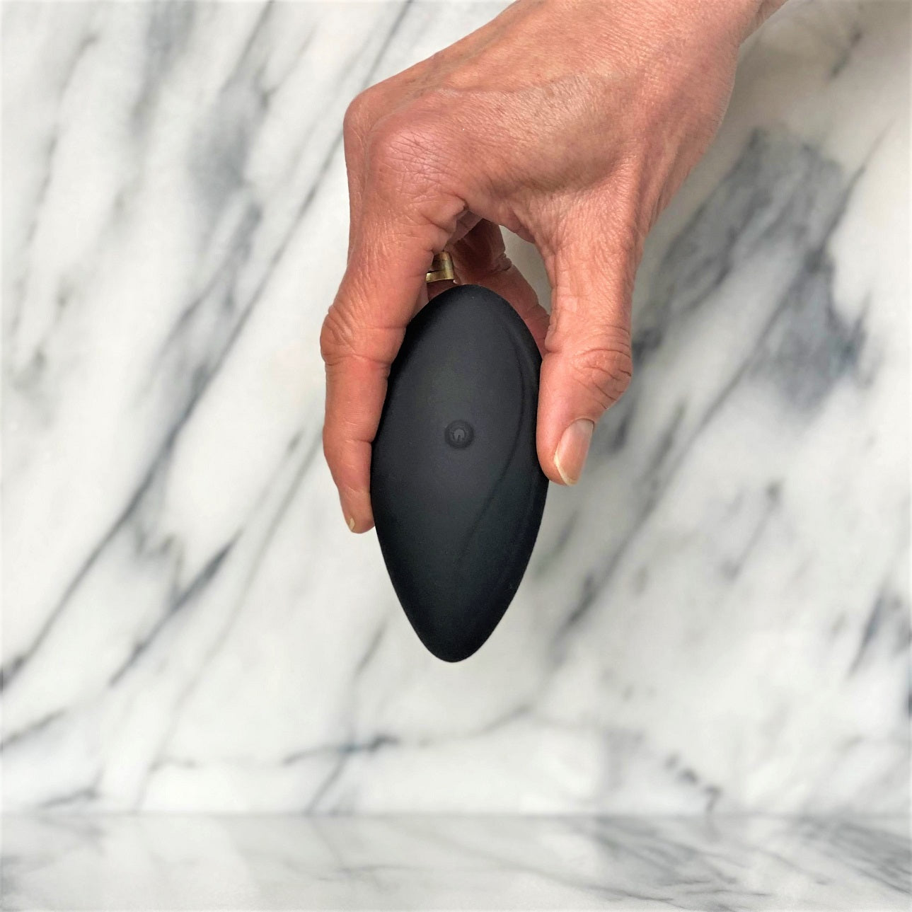 Hand houdt compacte zwarte Aludra stimulator vast met zichtbare bedieningsknop